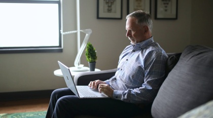 Man sits on couch in a living room looking at a laptop.